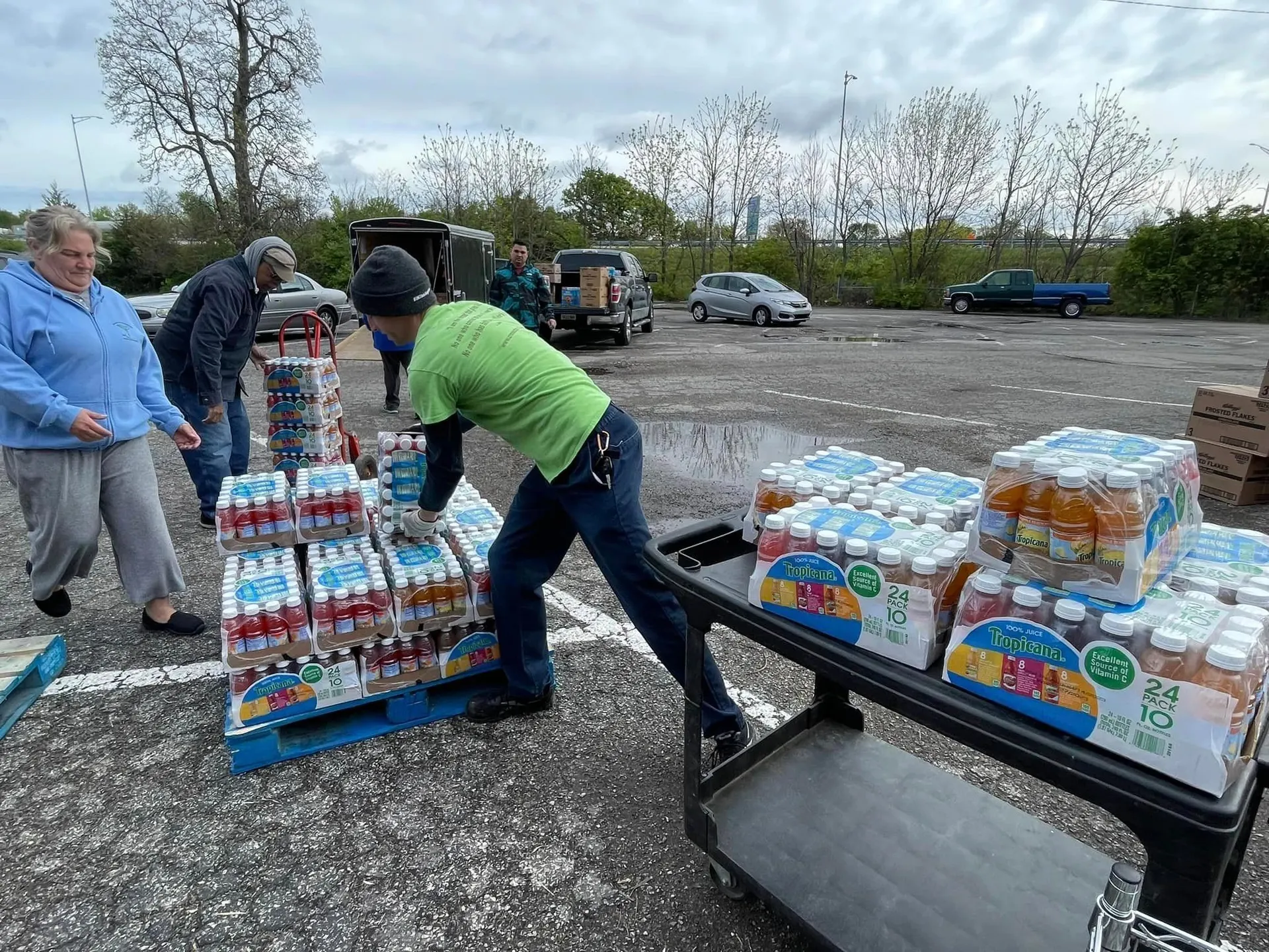 Volunteers moving pallets of juice and packaged food onto carts in a parking lot